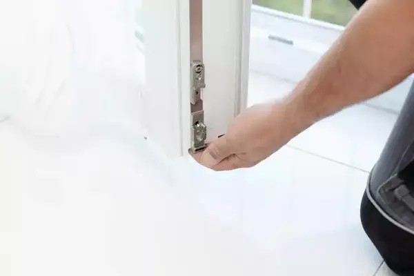 Ein Handwerker justiert das Scharnier an einem modernen weißen Fensterrahmen.