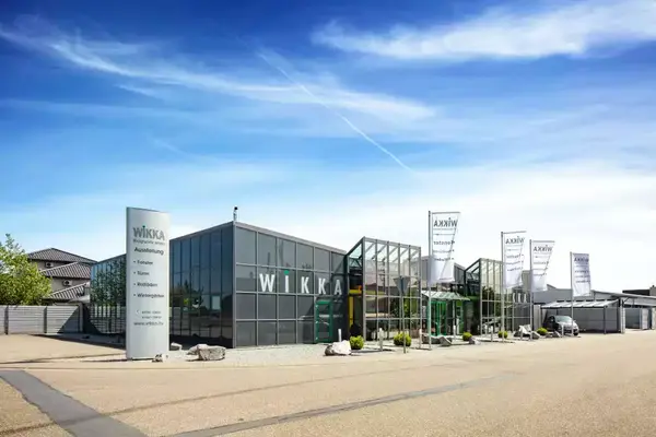 Modernes Firmengebäude von WIKKA mit Glasfassade, Ausstellungsbereich und Flaggen im Außenbereich.