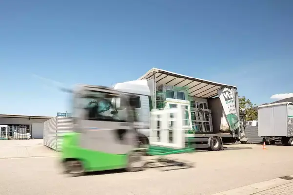 Ein Gabelstapler lädt Fenster auf einen LKW für den Fenstertransport bei Sonnenschein.