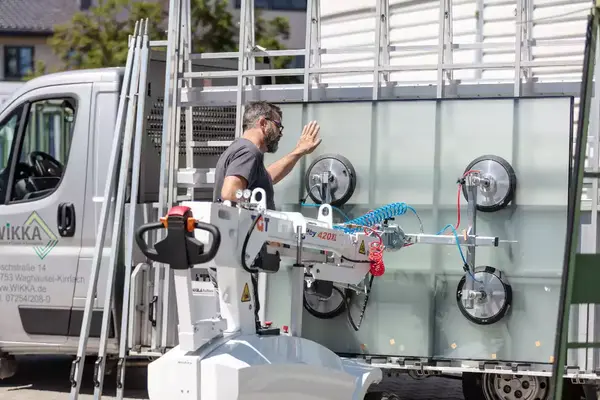 Ein Monteur setzt große Glasscheiben mit einem Vakuumheber vor einem Transporter ein.