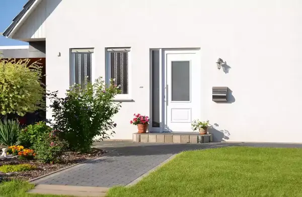 Moderner Hauseingang mit weißer Haustür, gepflegtem Vorgarten und Briefkasten.