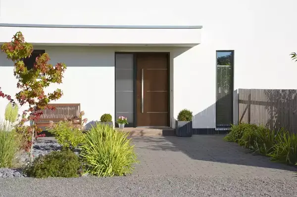 Moderner Hauseingang mit Holztür, Vorgarten, Pflanzen und Sitzbank bei Tageslicht.